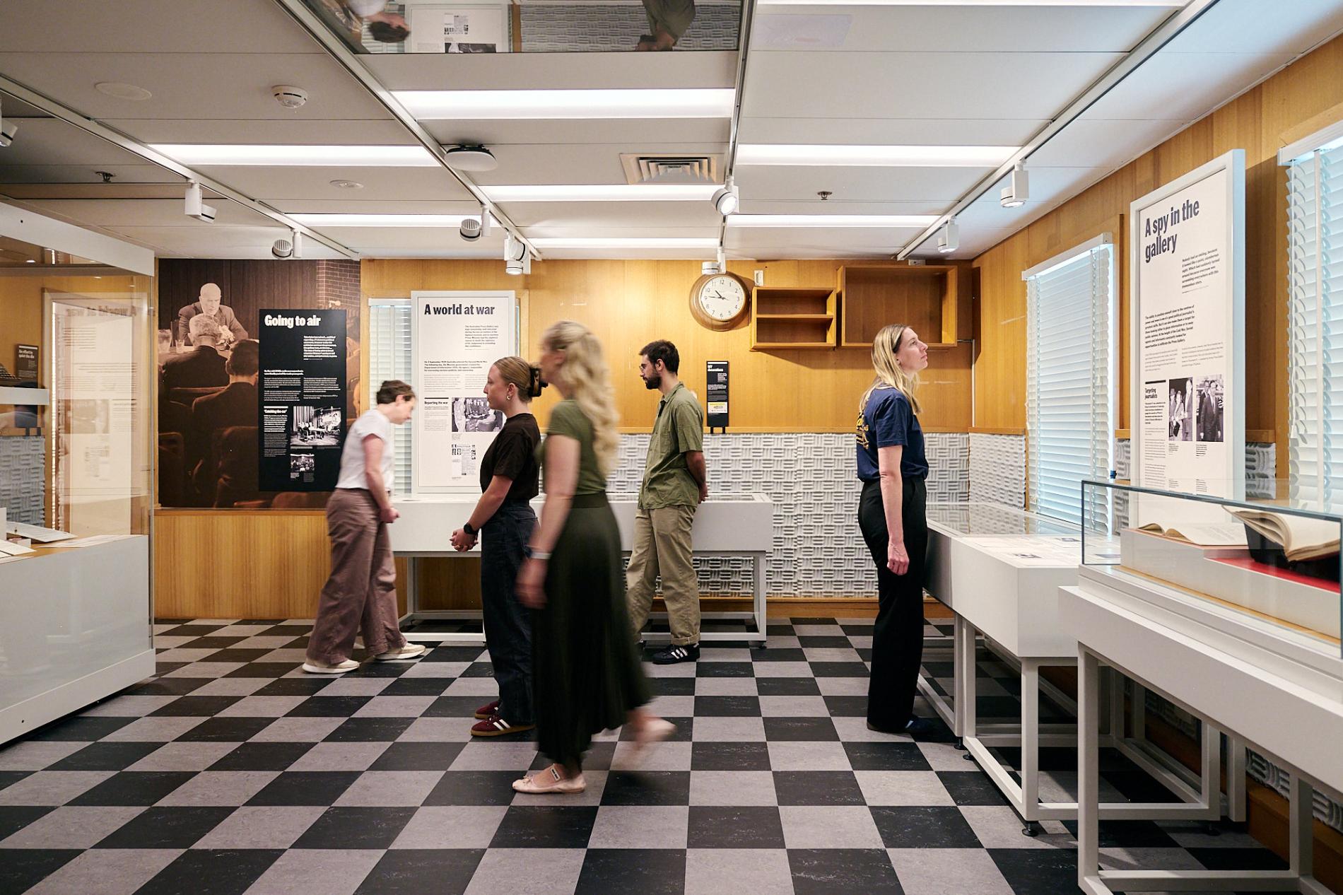 People stand on black and white tiled floor in the Press Gallery exhibition in Old Parliament House.