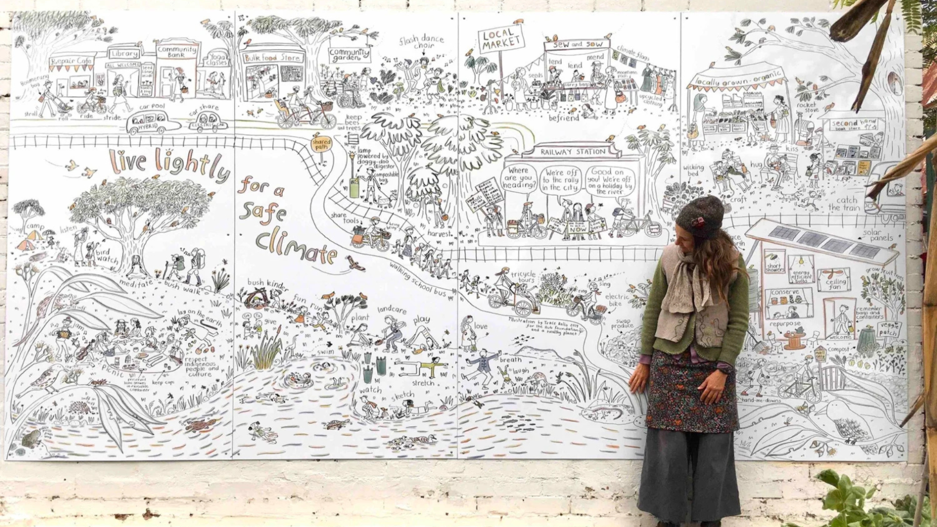 Trace Balla standing in front of a large mural illustration showing people living in nature. The mural is titled 'Live lightly for a safe climate'.