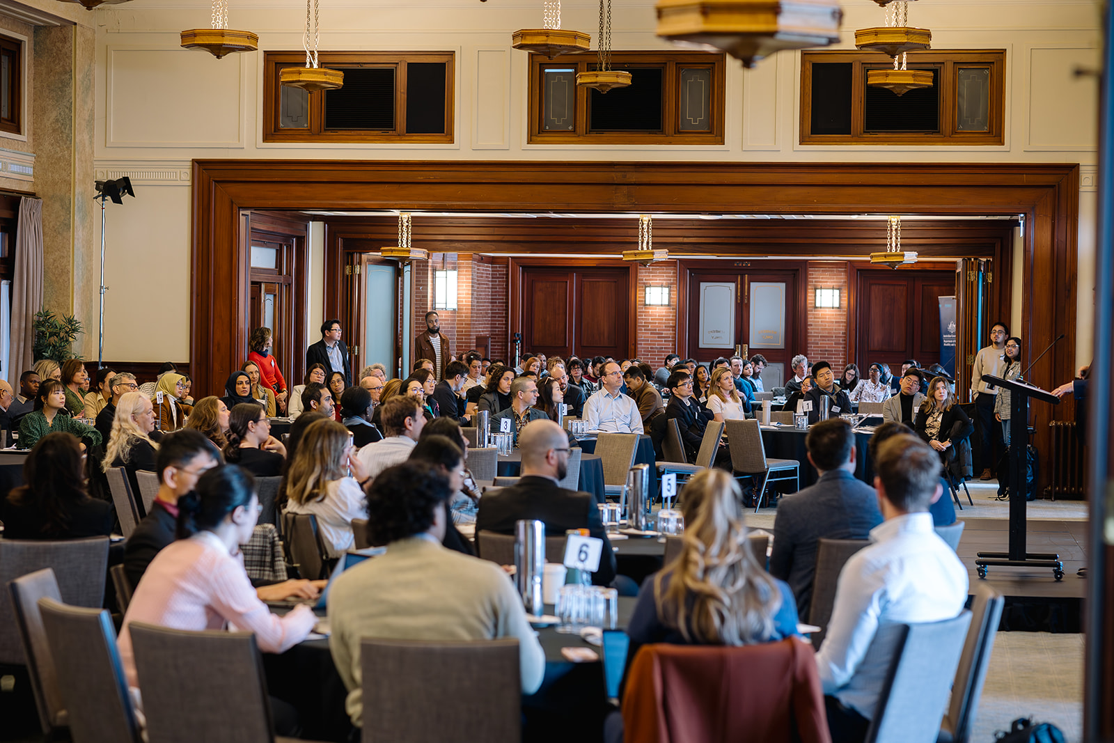 People seated at tables in the Member's Dining Room, facing a lectern where someone is giving a presentation.