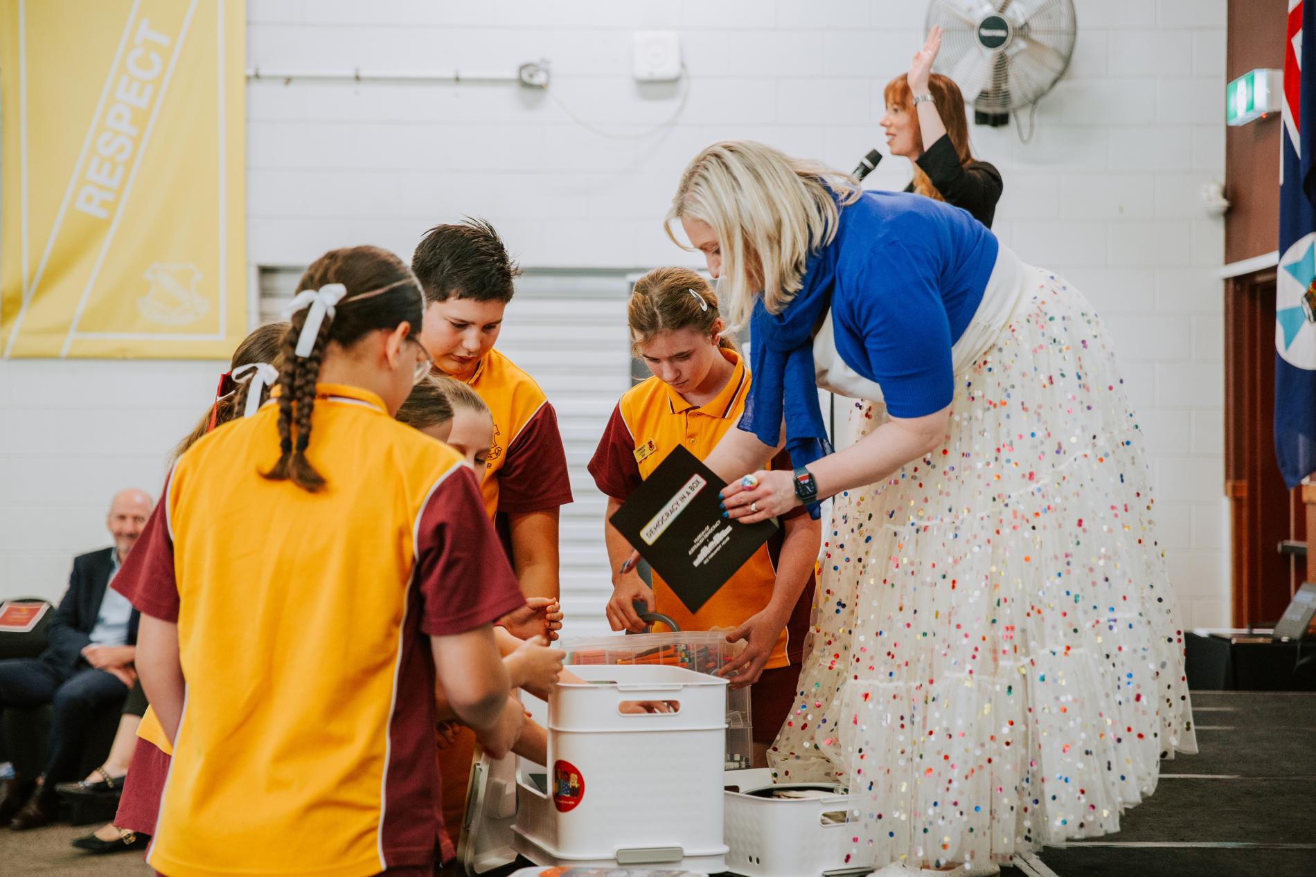 A small group of students in uniform, looking into the Democracy in a Box container with a teacher.