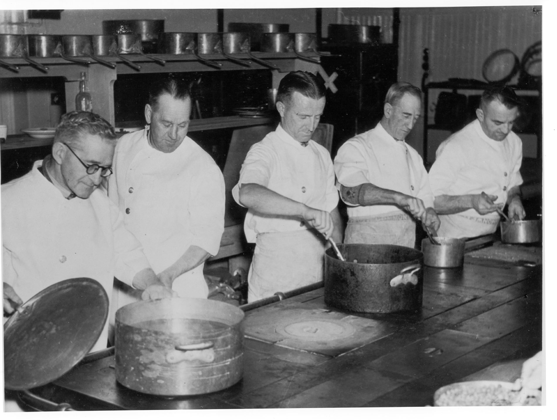 A black and white image of 5 cooks in uniforms on the line in the kitchen at Old Parliament House.