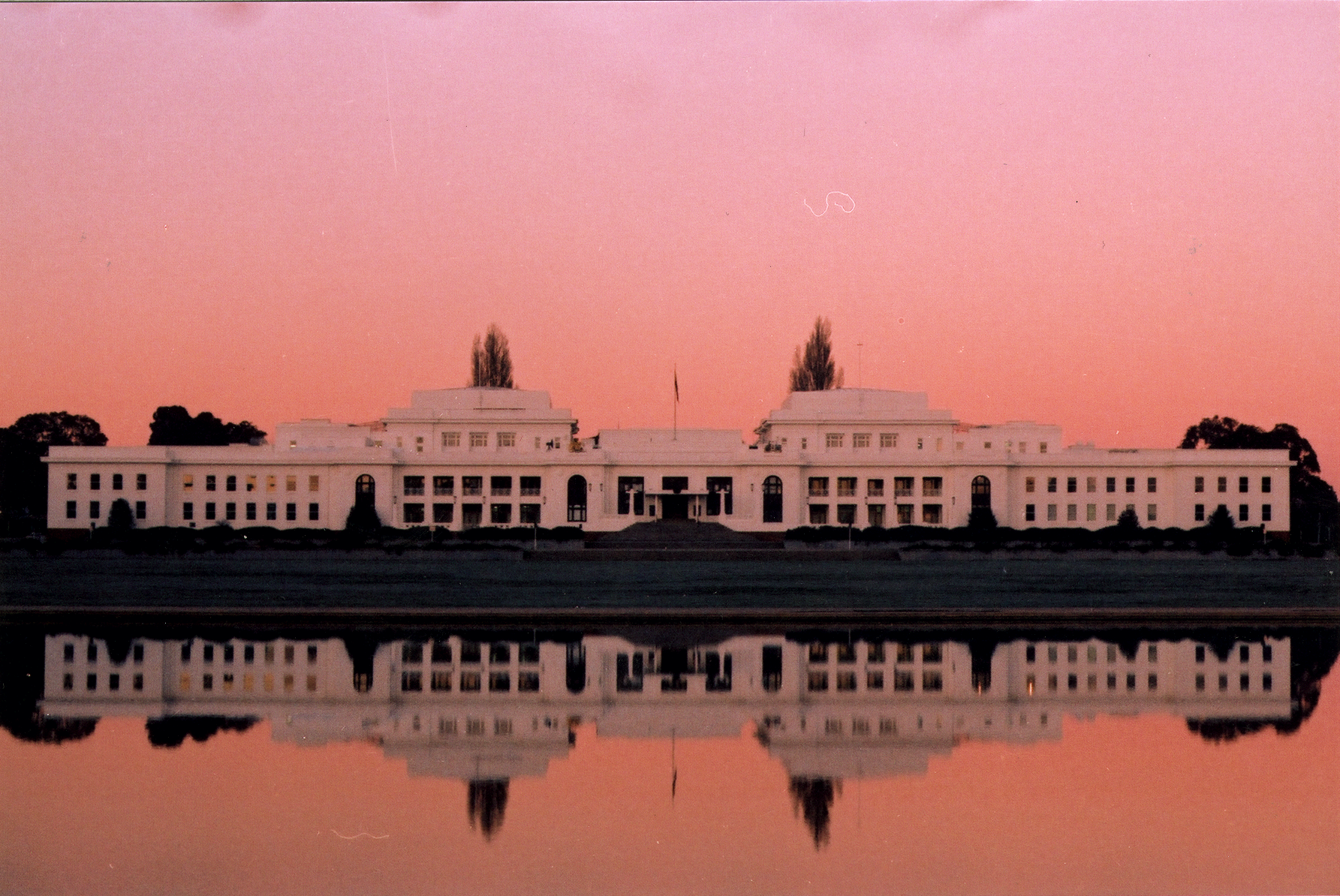 The front of Old Parliament House at sunset with a reflection seen clearly in a body of water.