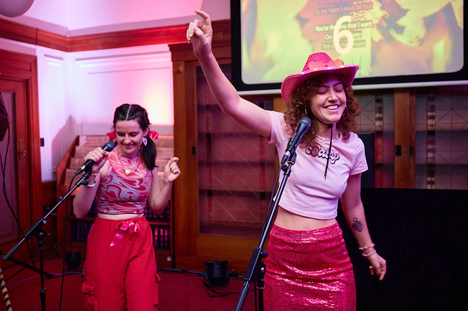 Two women wearing pink dance in front of microphones in Old Parliament House.