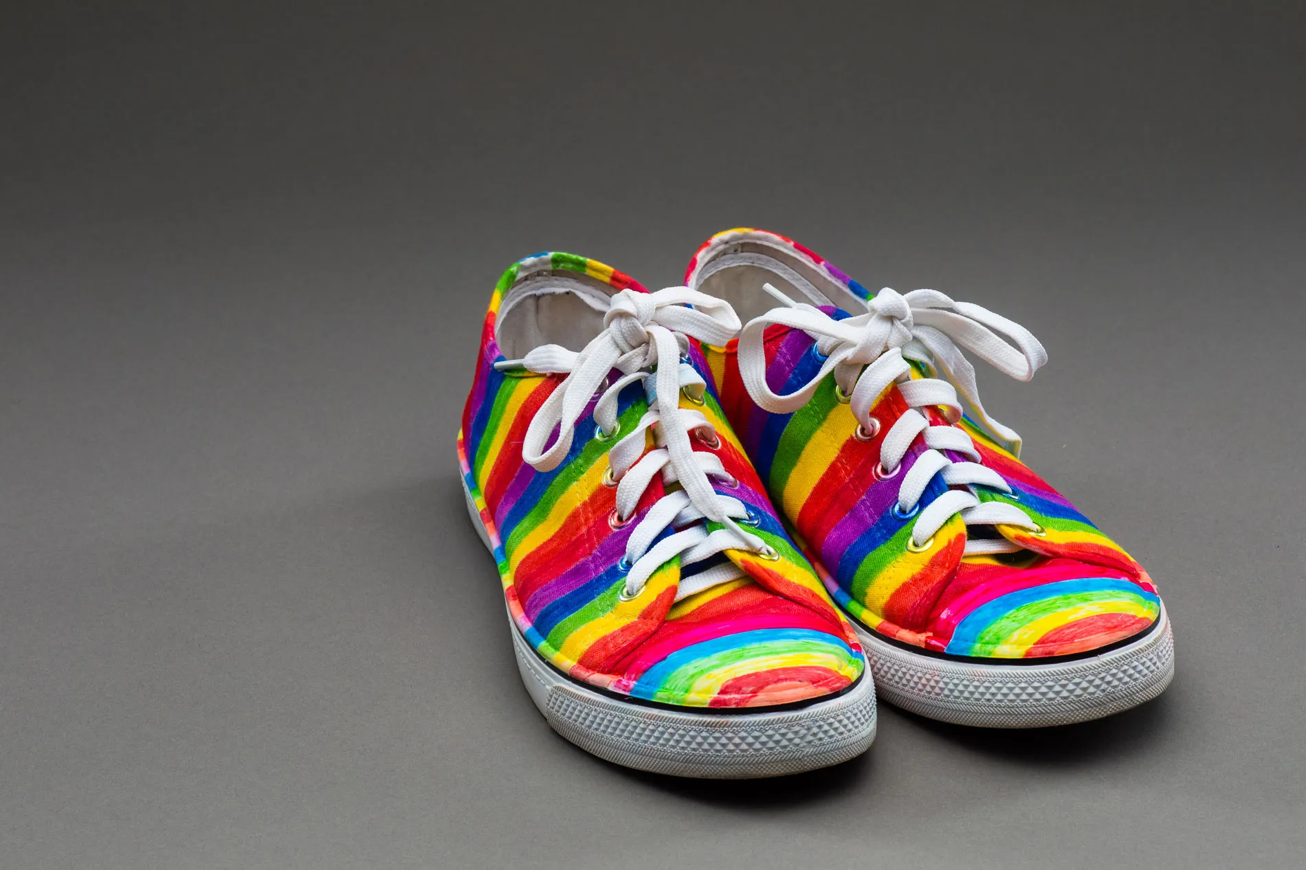 A pair of rainbow-painted sneakers with white laces. A pair of rainbow-painted sneakers with white laces.