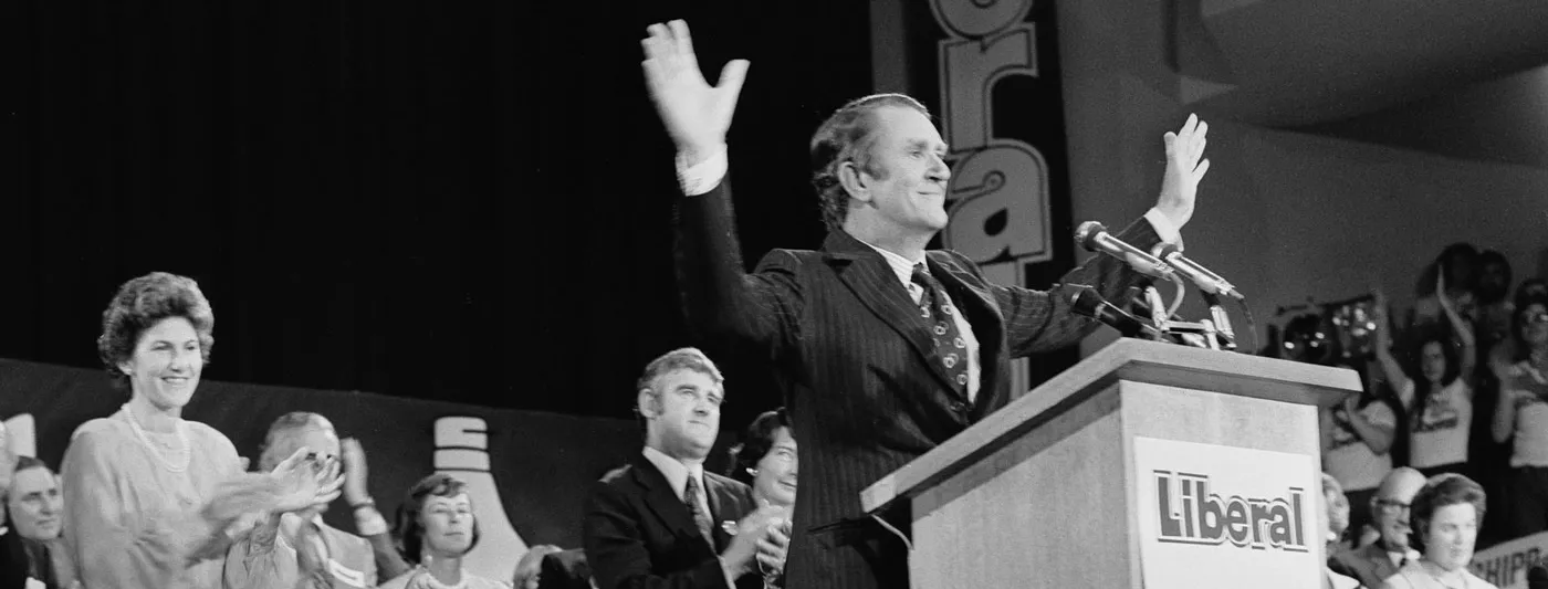 Malcolm Fraser stands at a podium on stage at a Liberal campaign rally.