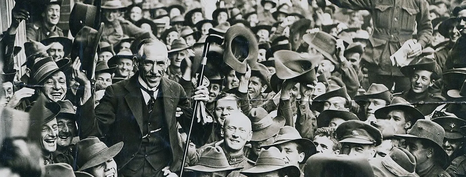 Prime Minister Billy Hughes is carried by soliders through a crowded street.