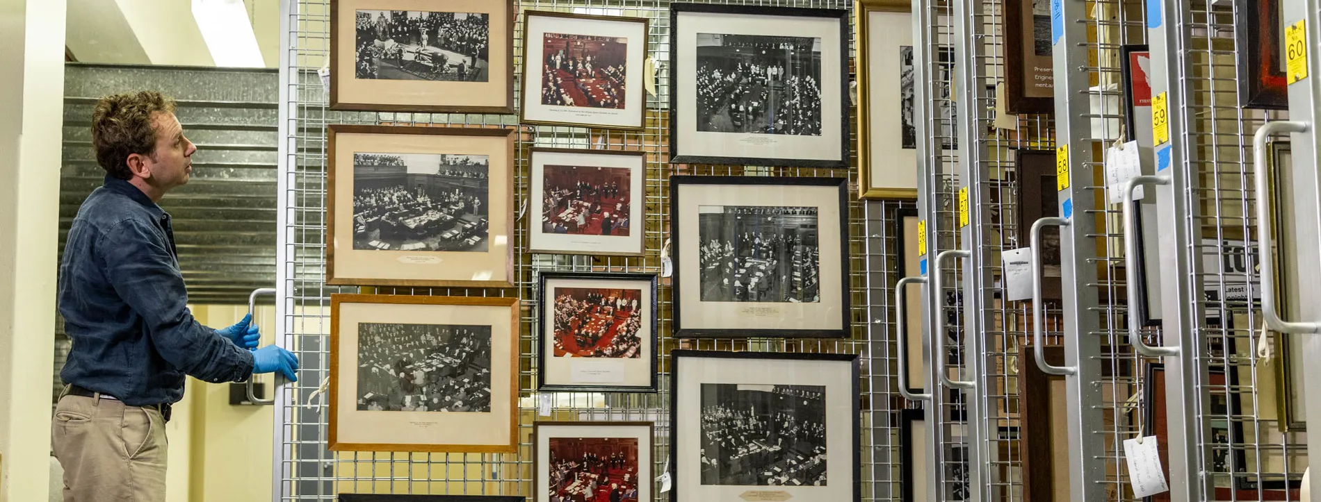 A man pulls a sliding storage display featuring framed pictures in Old Parliament House.