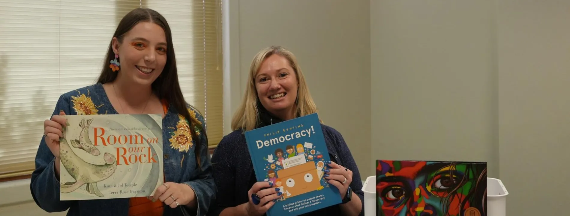 Two women hold up picture books in a room in Old Parliament House.