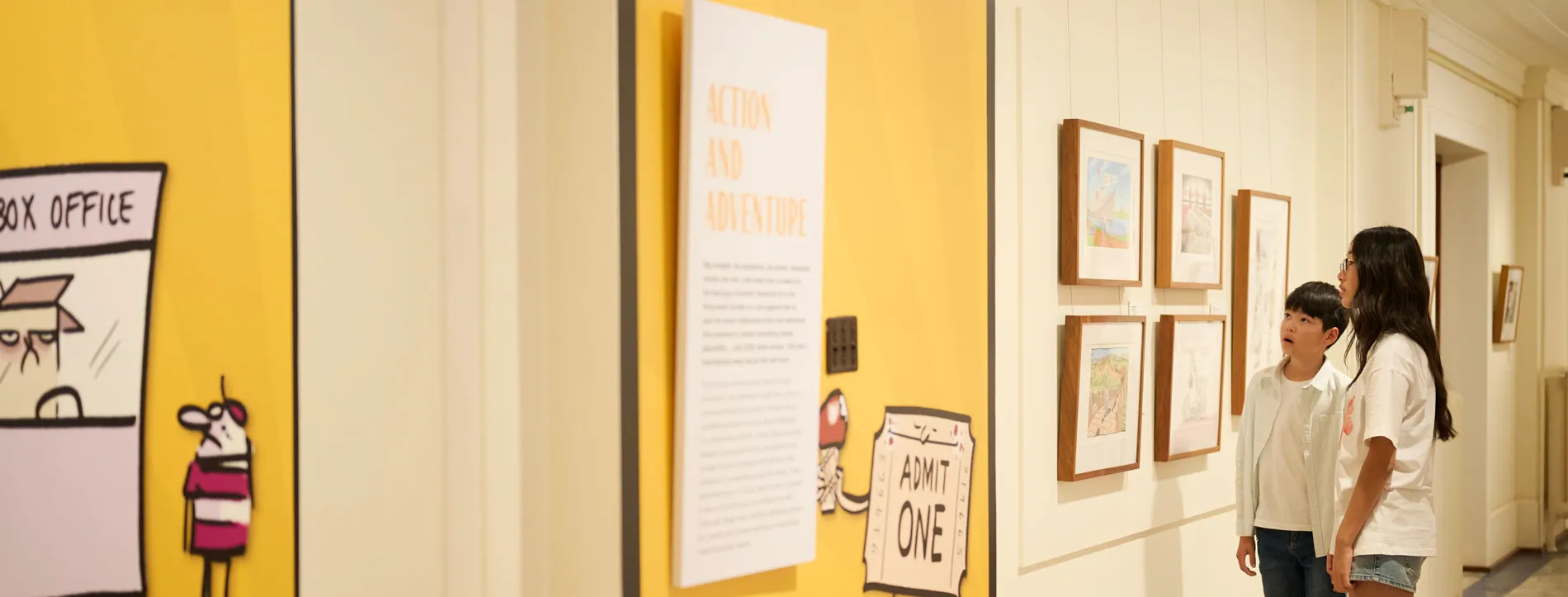 Two kids look at a wall of political cartoons in Old Parliament House.