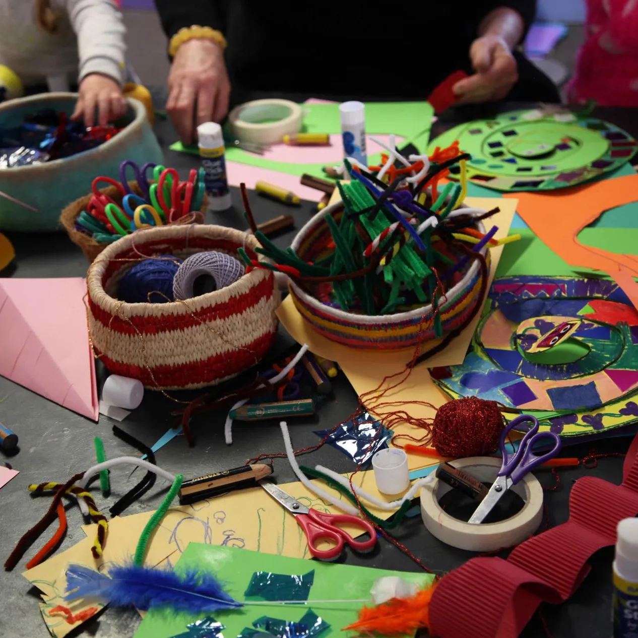 A table covered in coloured paper, feathers, scissors, glue, string and craft supplies. 