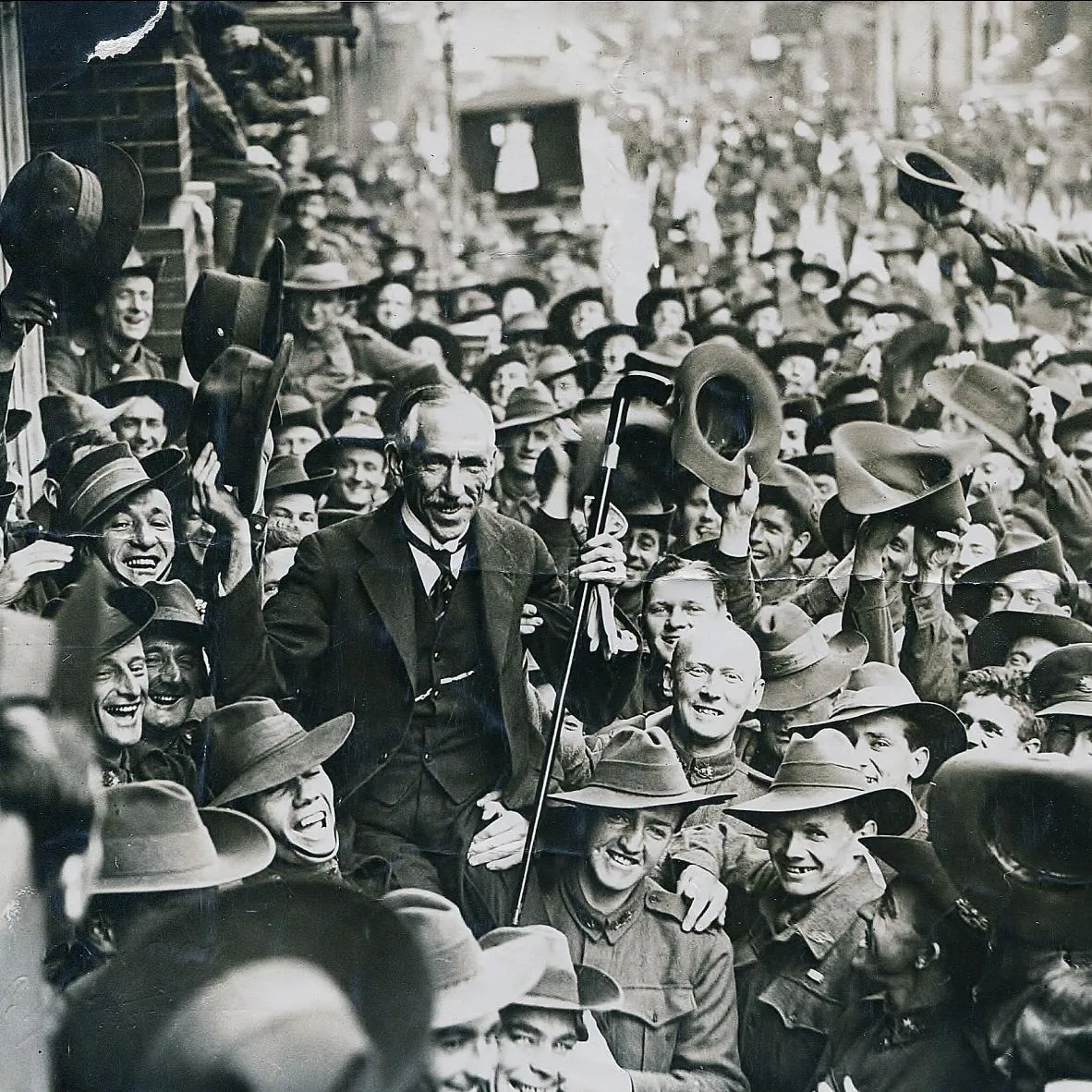 Prime Minister Billy Hughes is carried by soliders through a crowded street.