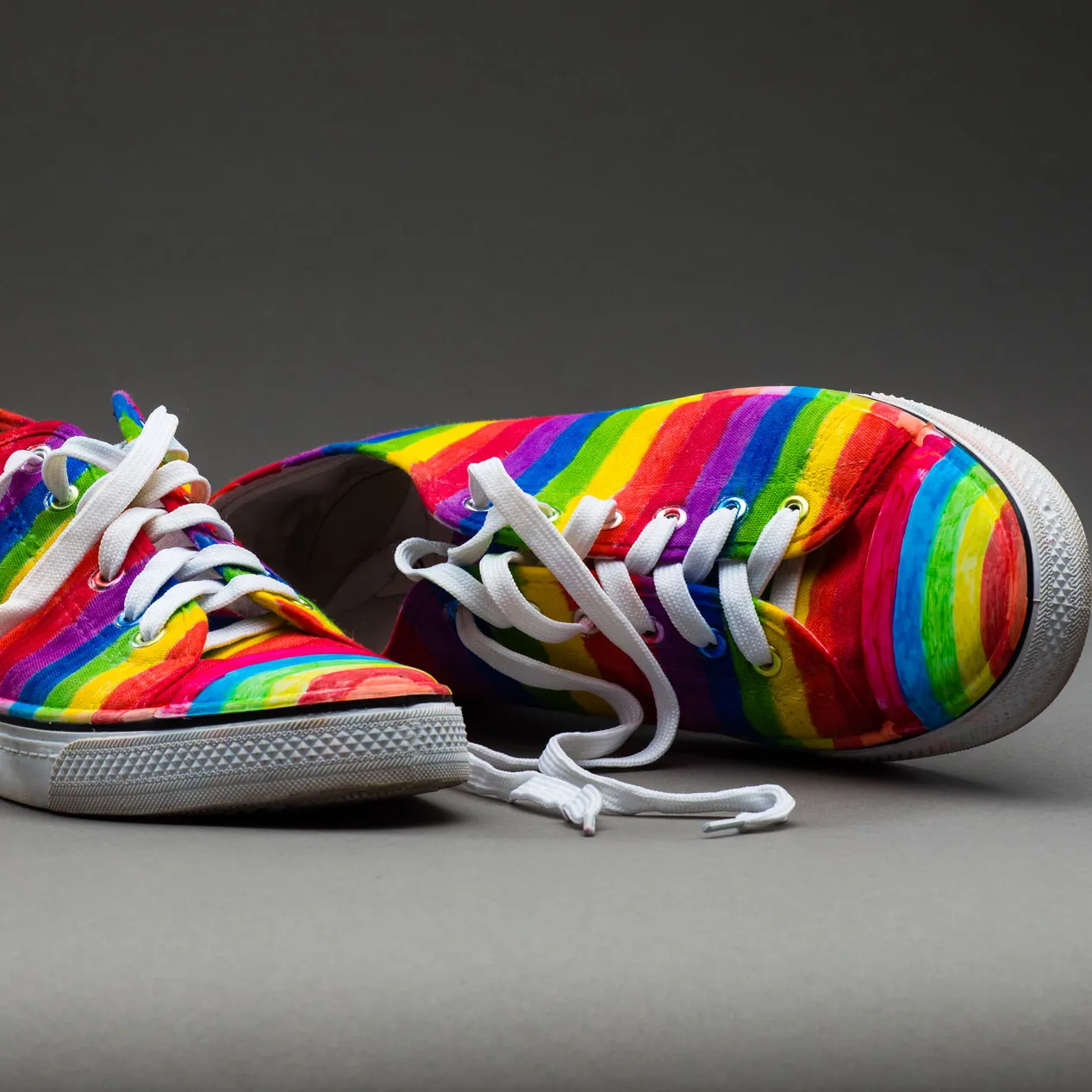 A pair of sneakers painted with rainbow stripes.