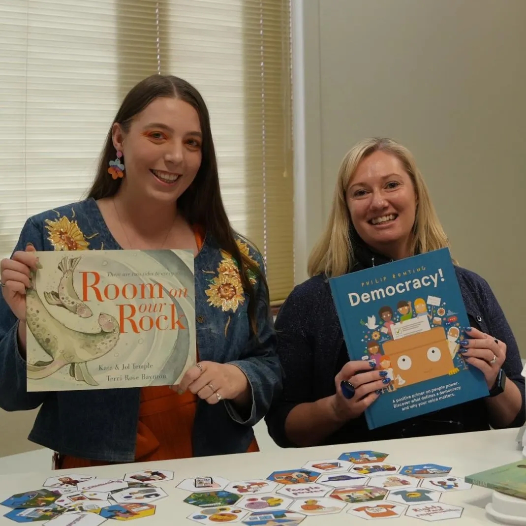 Two women hold up picture books in a room in Old Parliament House.