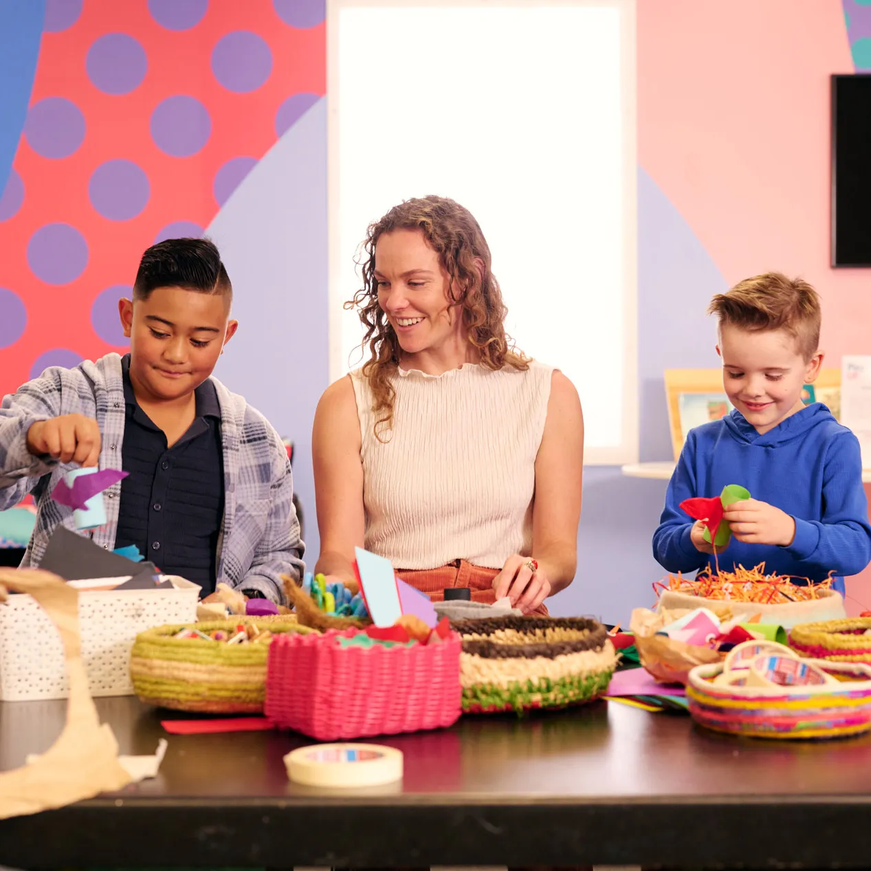 Two kids and a woman craft at a table filled with colourful baskets at Old Parliament House.