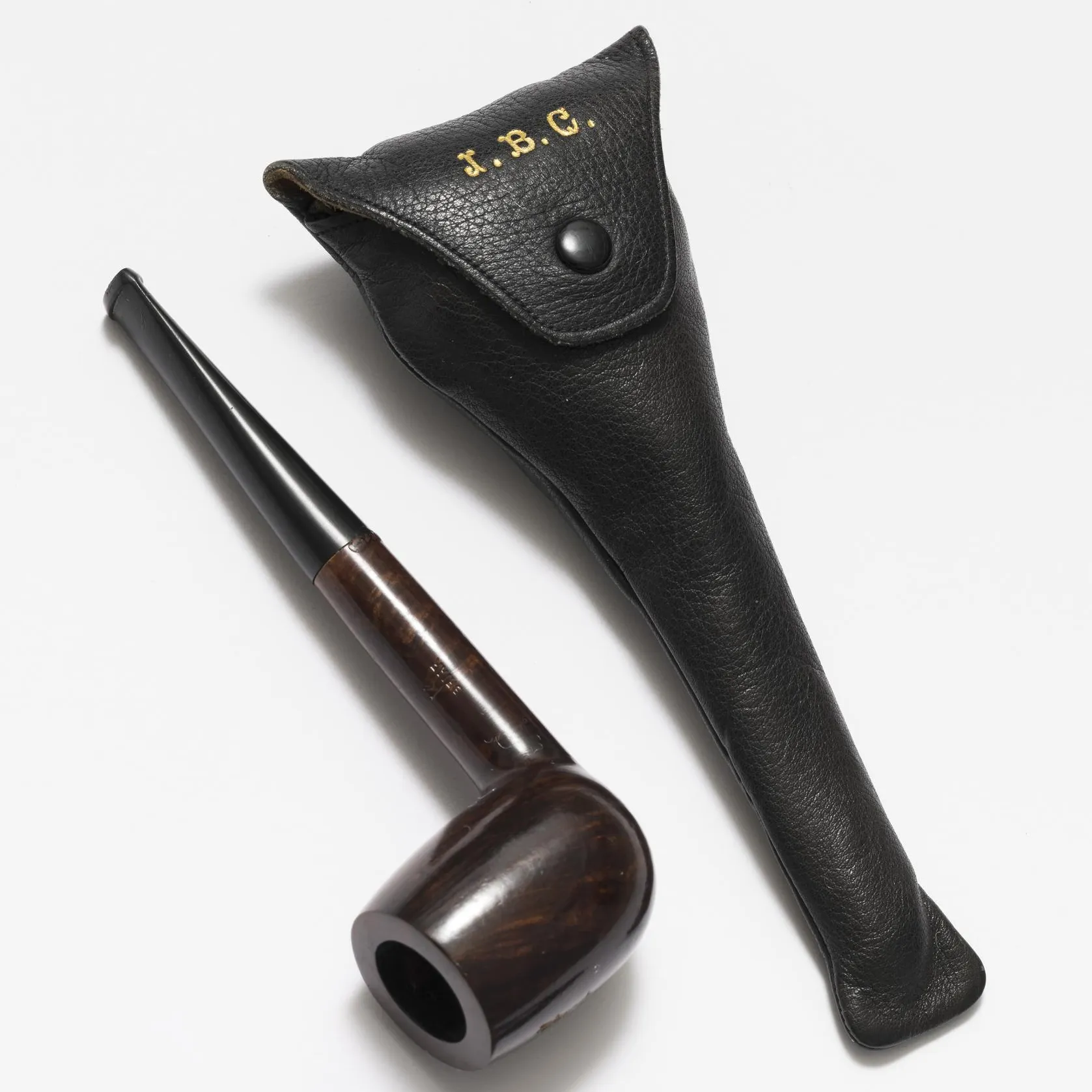 An old tobacco pipe that belonged to Ben Chifley next to its case. The case features golden lettering of the initials J. B. C.