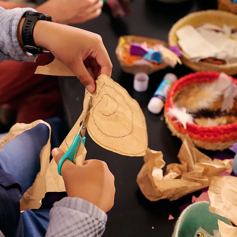 A child uses aqua scissors to cut out a shape above a craft table.