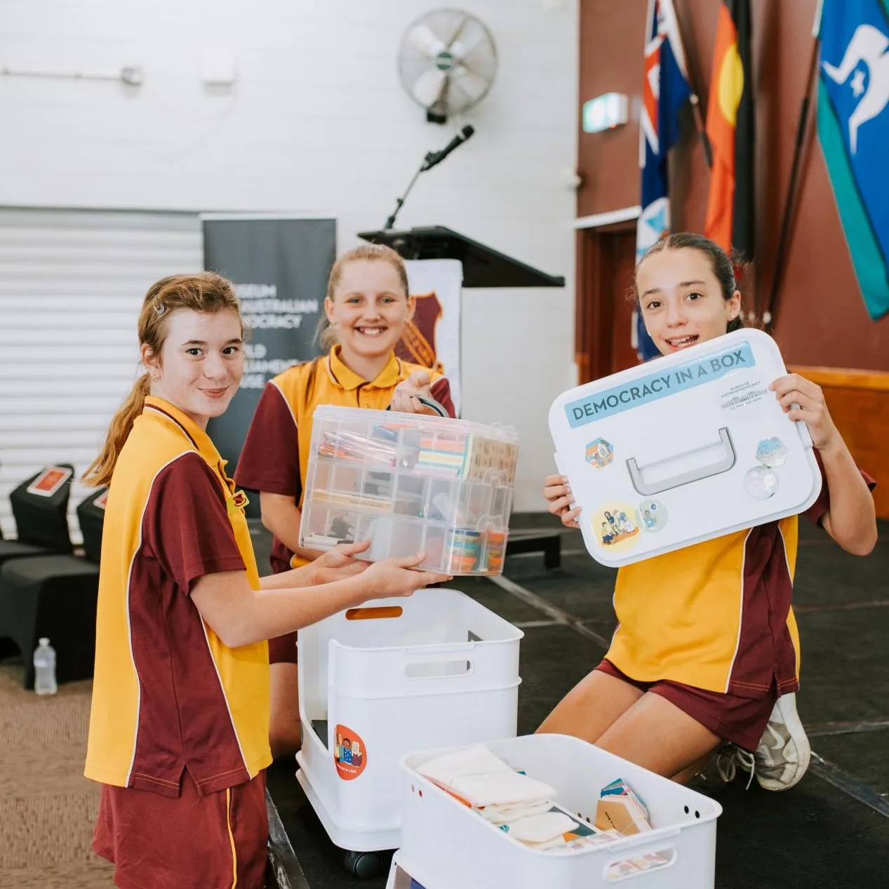 Three students in uniform engaging with Democracy in a box in a school hall.