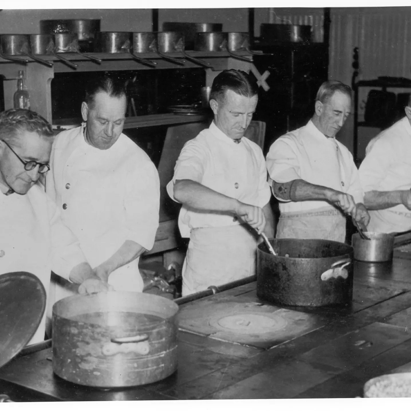 A black and white image of 5 cooks in uniforms on the line in the kitchen at Old Parliament House.