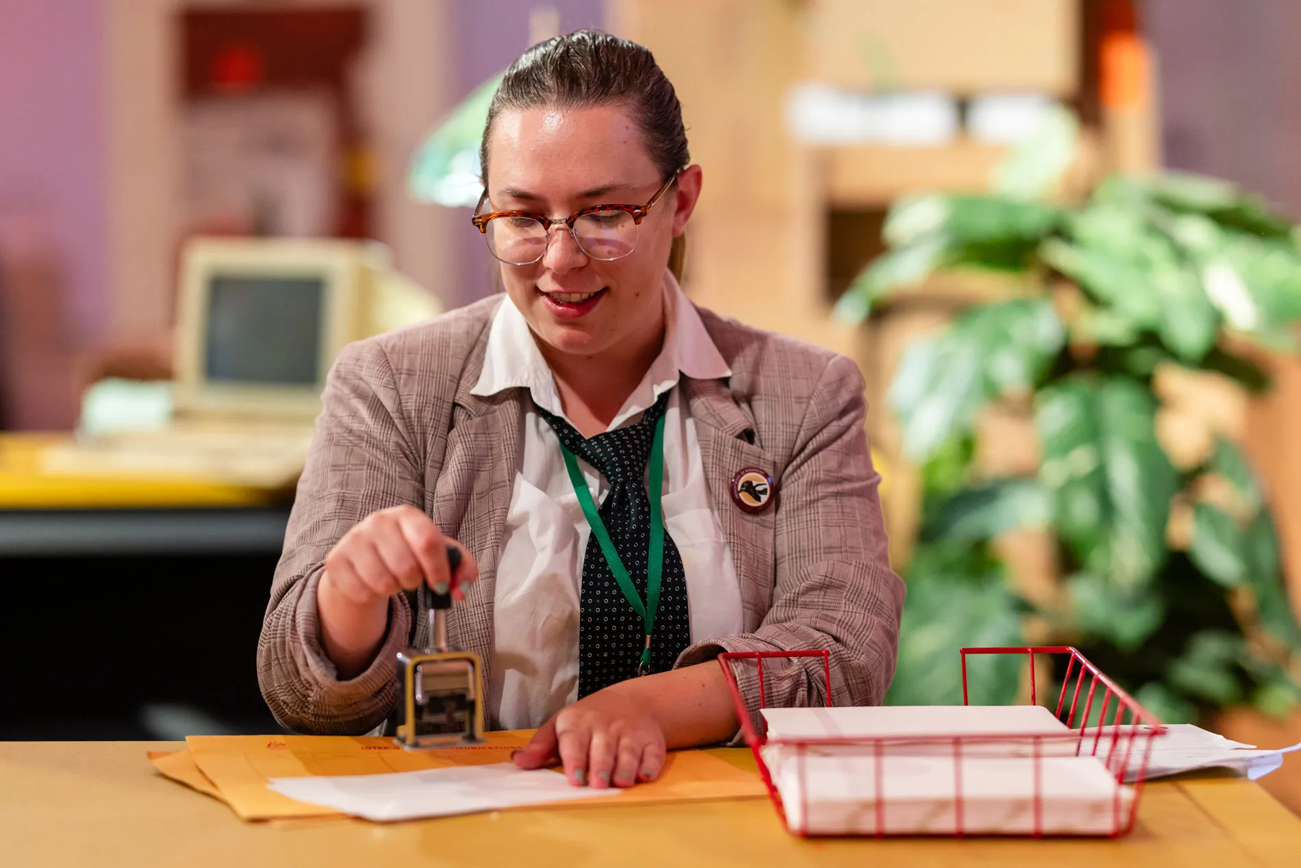 A woman in a blazer and tie stamps a yellow folder at a desk in Old Parliament House.