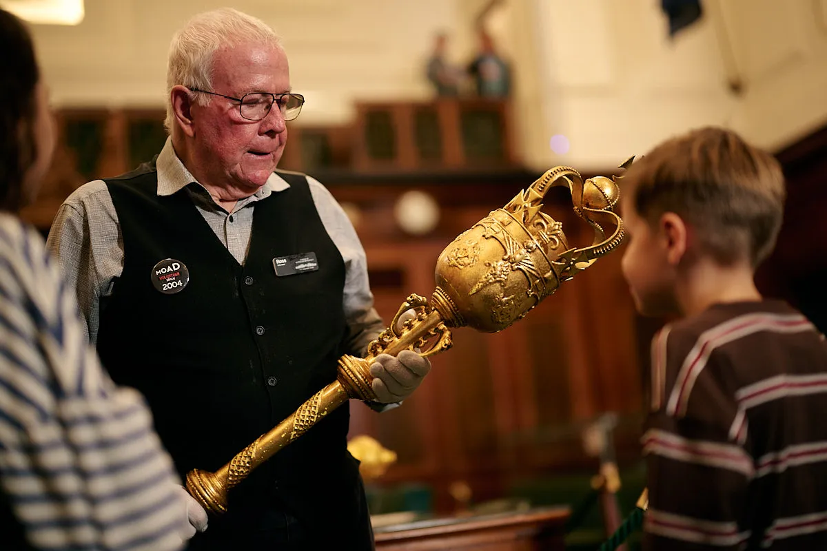A volunteer at the Museum of Australian Democracy showing some children a golden replica mace in the House of Representatives chamber.