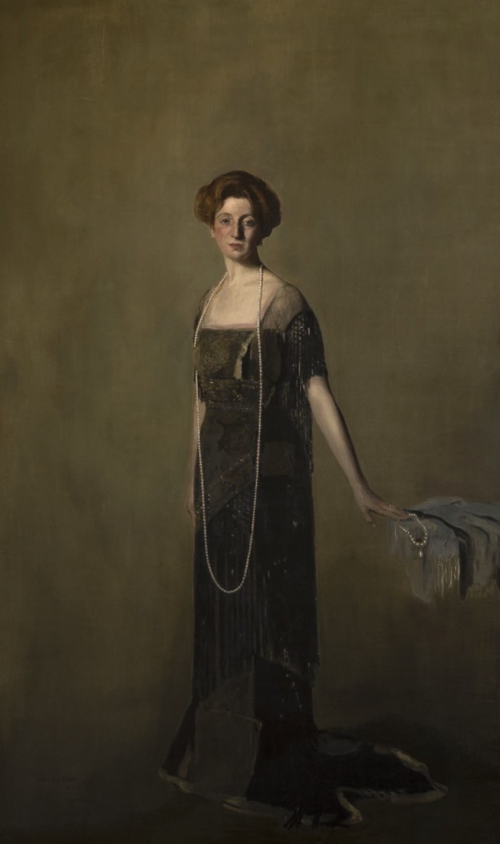 Lady Denman, with short brown hair, wearing a long dark dress and a long pearl necklace that drapes down to knee height.