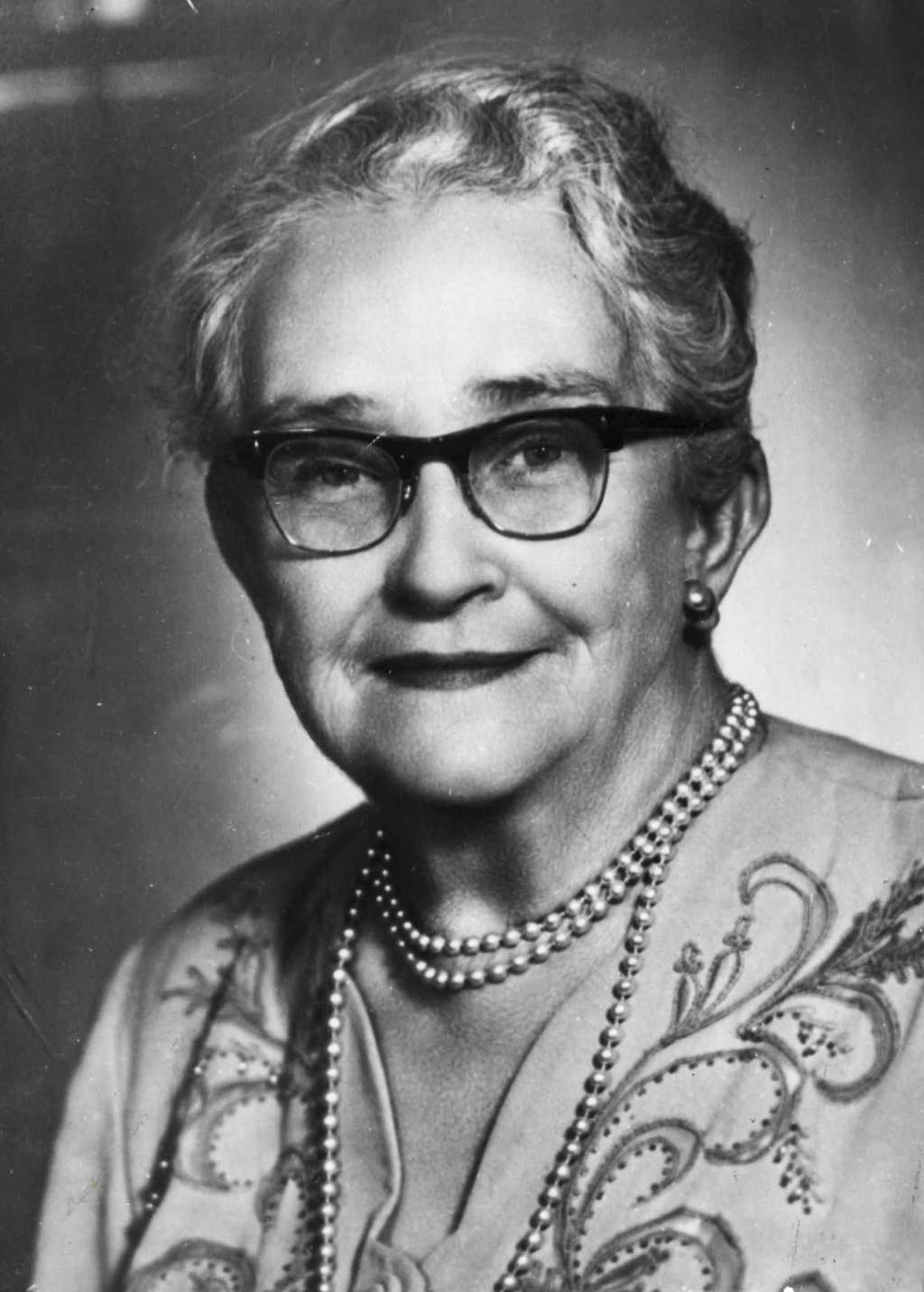 Senator Agnes Robertson, wearing thick-rimmed glasses and pearl earrings and necklace.