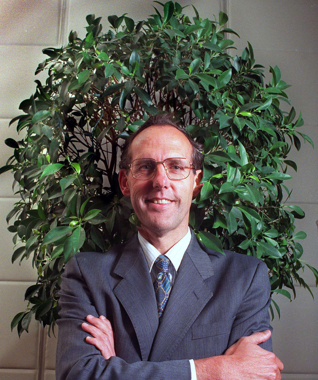 Dr Bob Brown, posing arms crossed in front of a small tree.