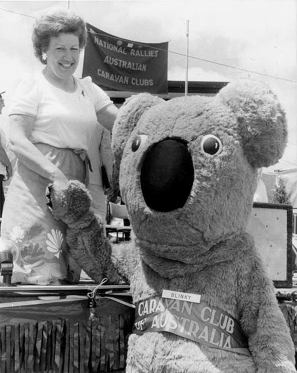 Senator Margaret Reid shakes hands with a person wearing a large koala costume with the nametag 'Blinky'.