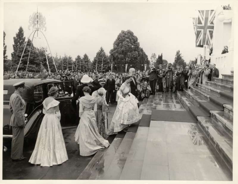 Queen Elizabeth walks up the stairs of Old Parliament House in 1954, wearing a formal gown and surrounded by people. 