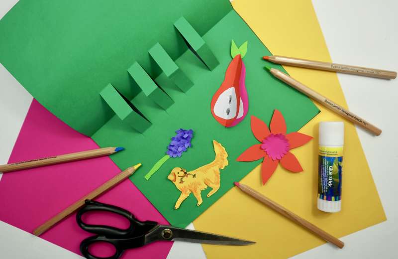 A green piece of paper with glue, pencils, textas and paper decorations. 