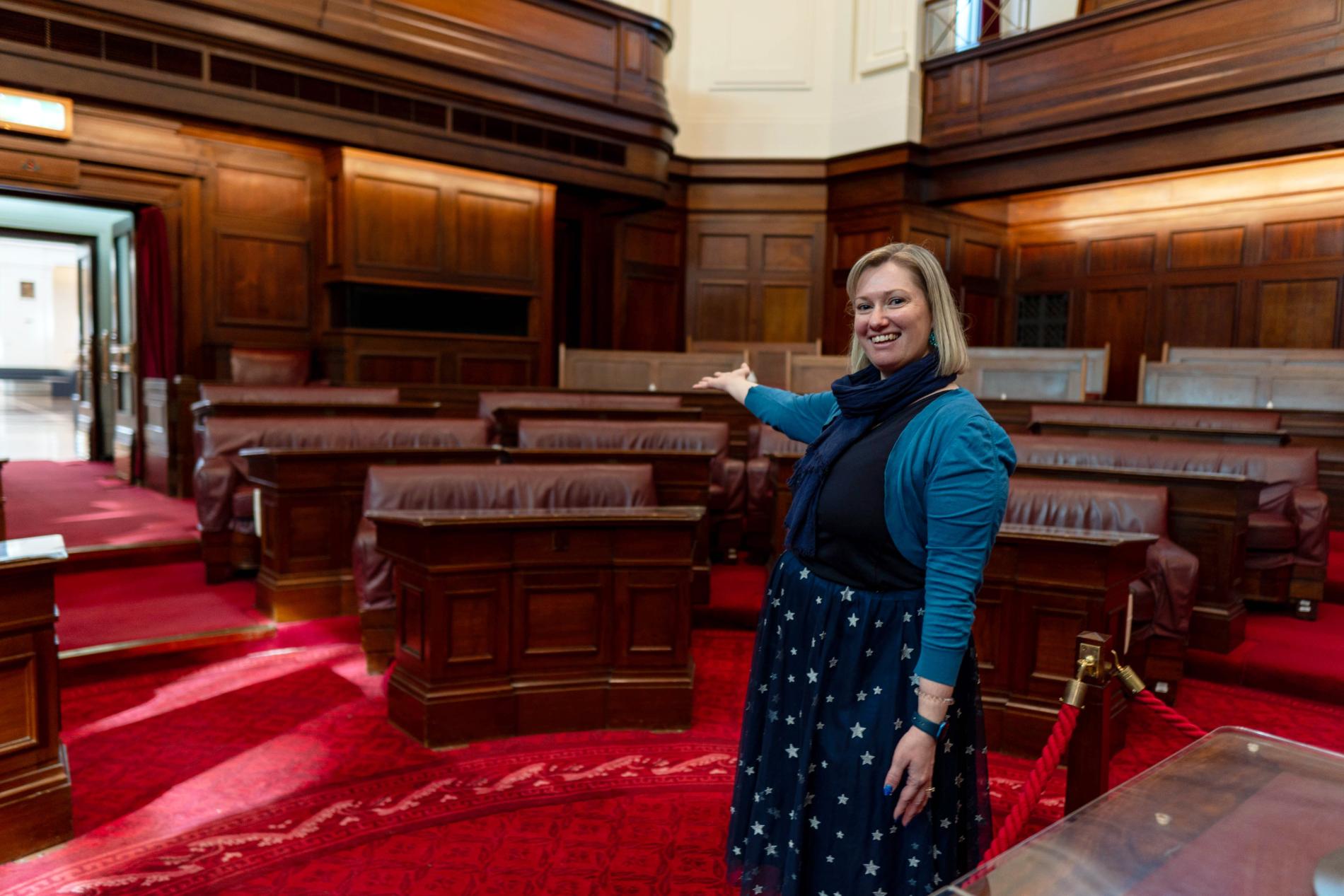 A person stands with their arm outstreched in the senate chamber at old parliament house