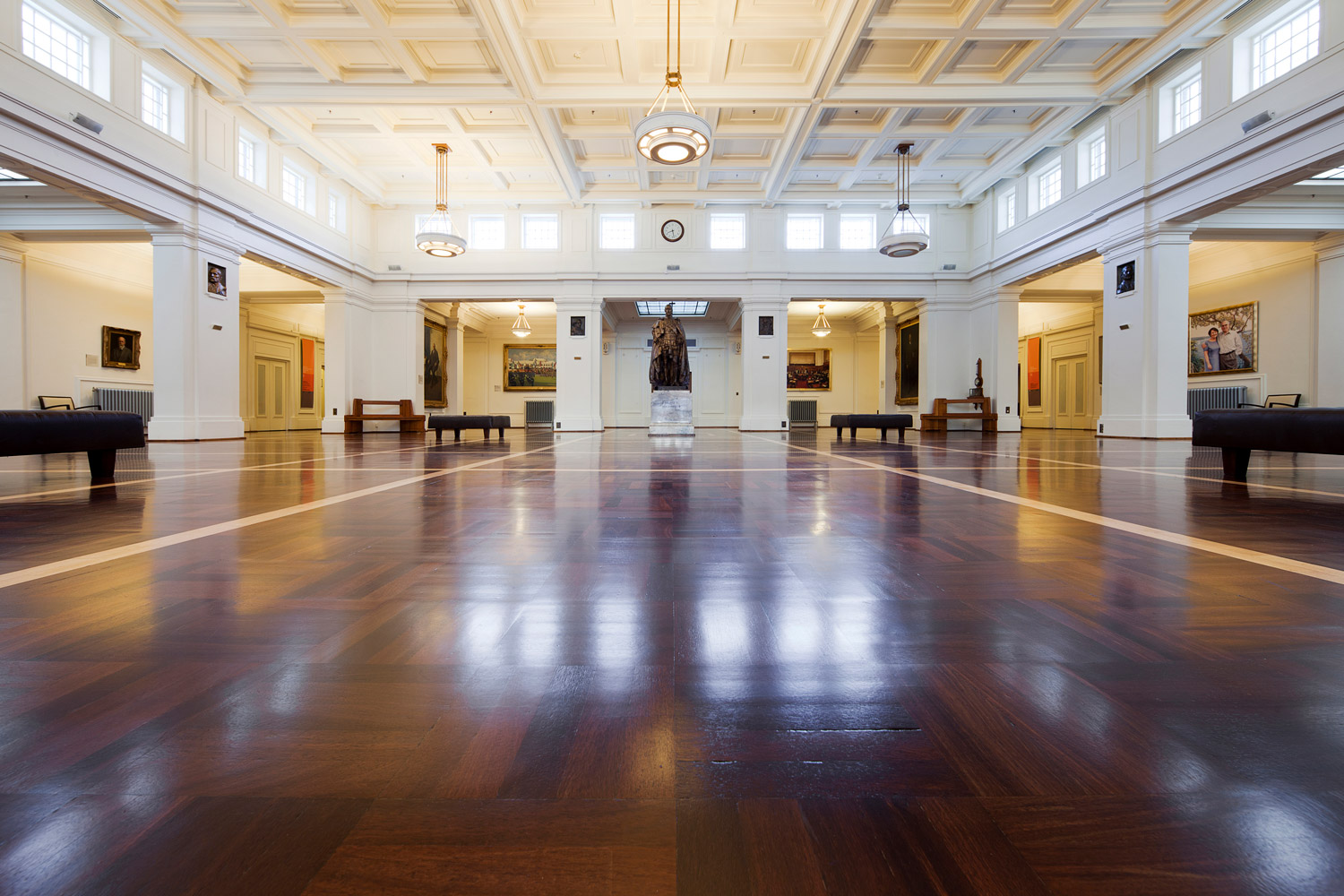 Photograph of a large room with wooden flooring, white walls and ceiling, and a statue of King Geroge V at the centre back.  