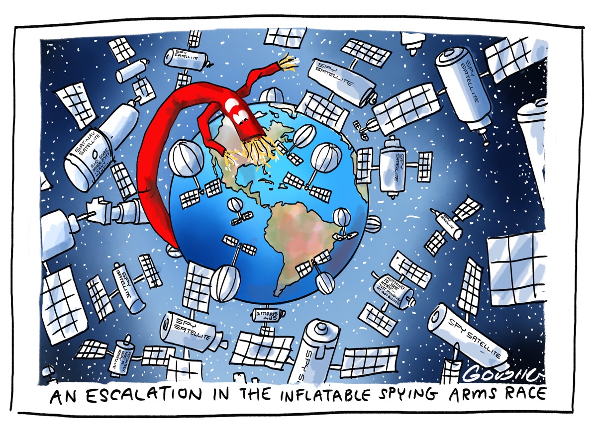 Earth is surrounded by a variety of space satellites. An red inflatable tube with a face and long arms looms over North America. Text reads: 'An escalation in the inflatable spying arms race'.