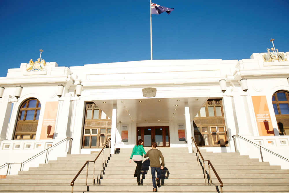 Two people walk up the front entrance steps of Old Parliament House.