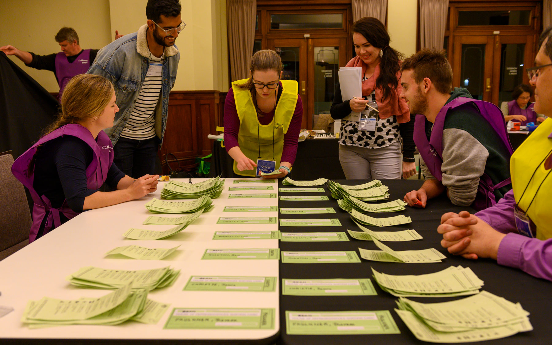 Officials in yellow and purple vests count green ballot paper votes on a table in Old Parliament House.