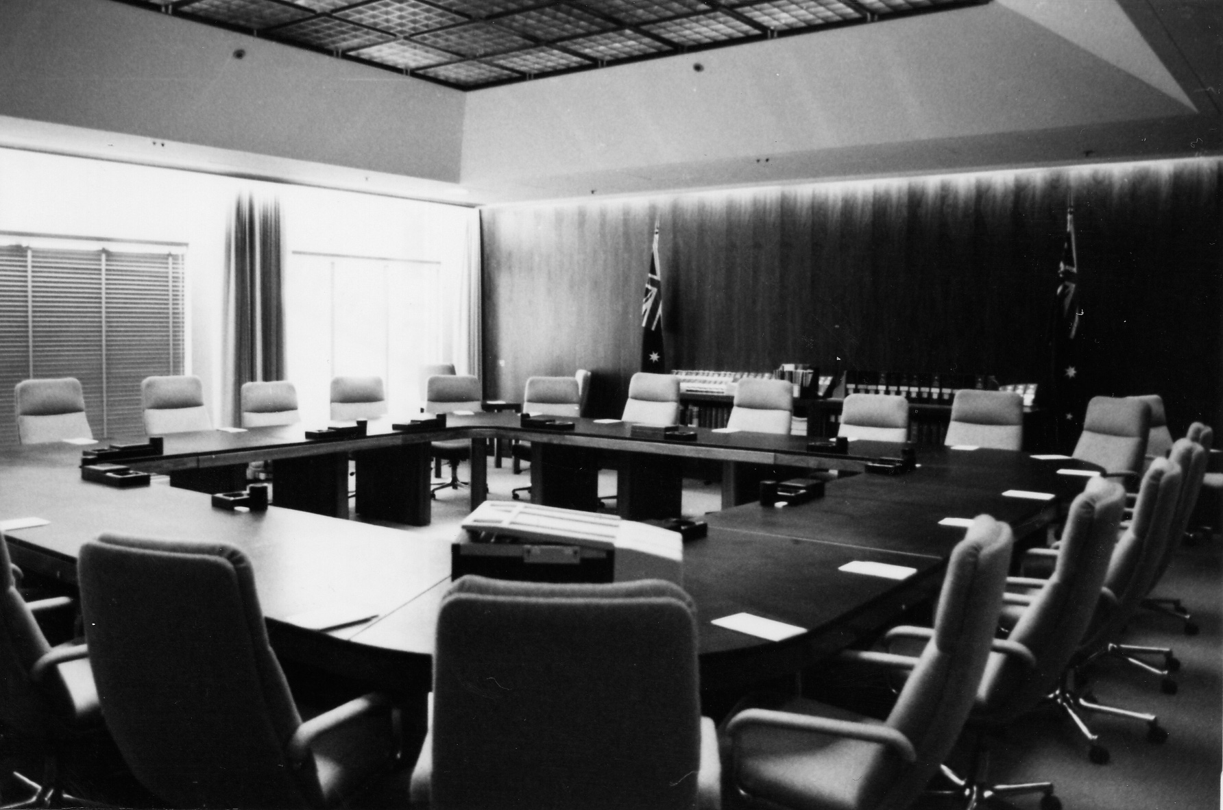 The Cabinet Room at Old Parliament House with a square table surrounded by chairs. Two Australian flags stand along a wood panelled wall.