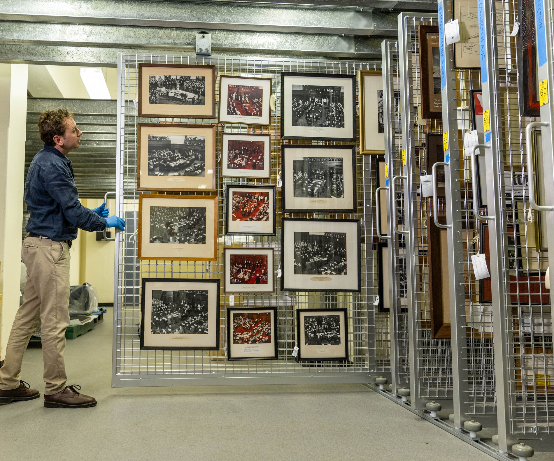 A man pulls a sliding storage display featuring framed pictures in Old Parliament House.