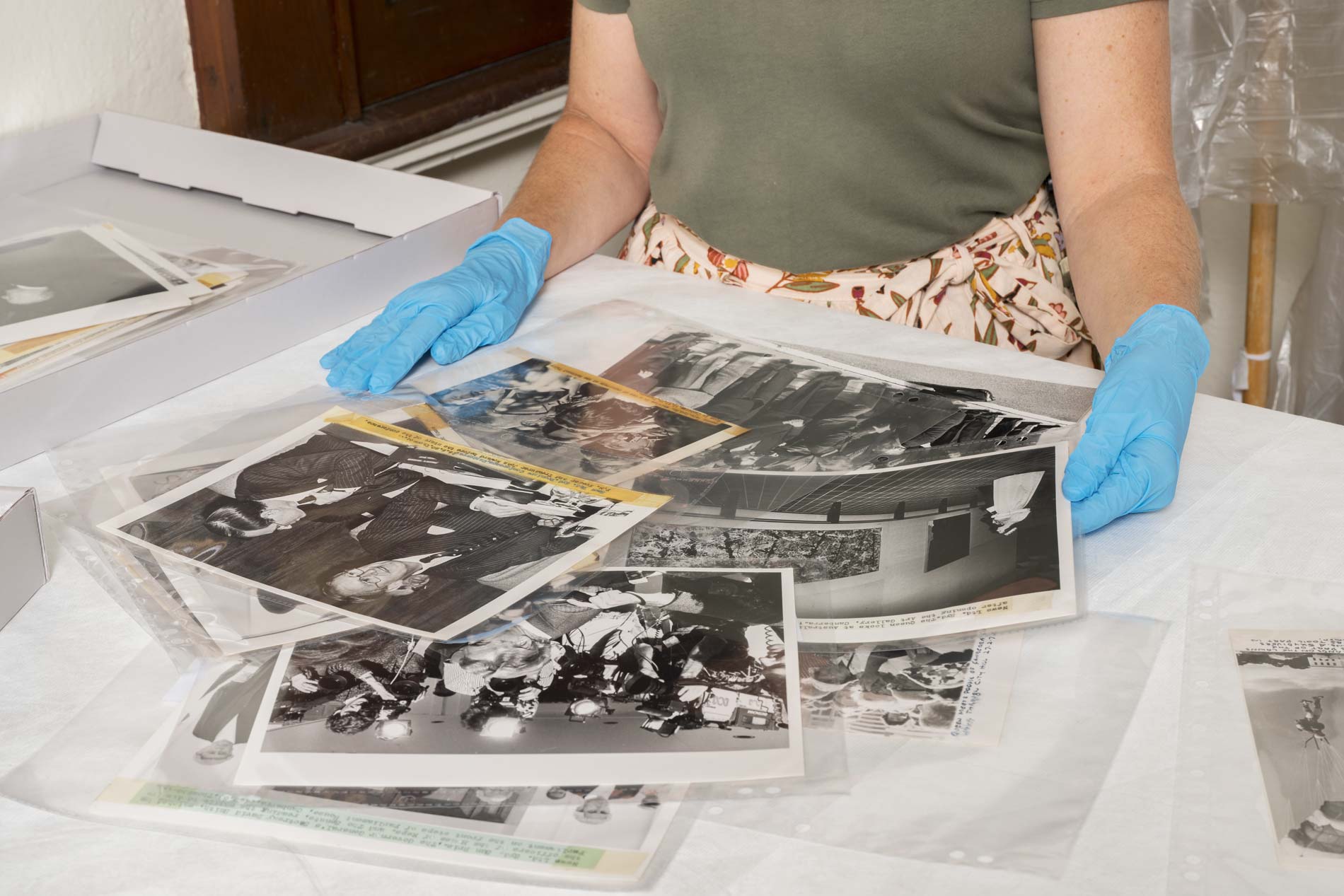 A person wearing blue gloves sorts black and white photographs on a desk. 