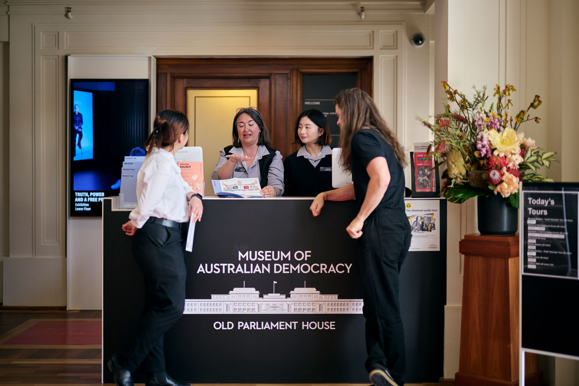 Museum staff show visitors to a brochure at the reception desk at MoAD at Old Parliament House.