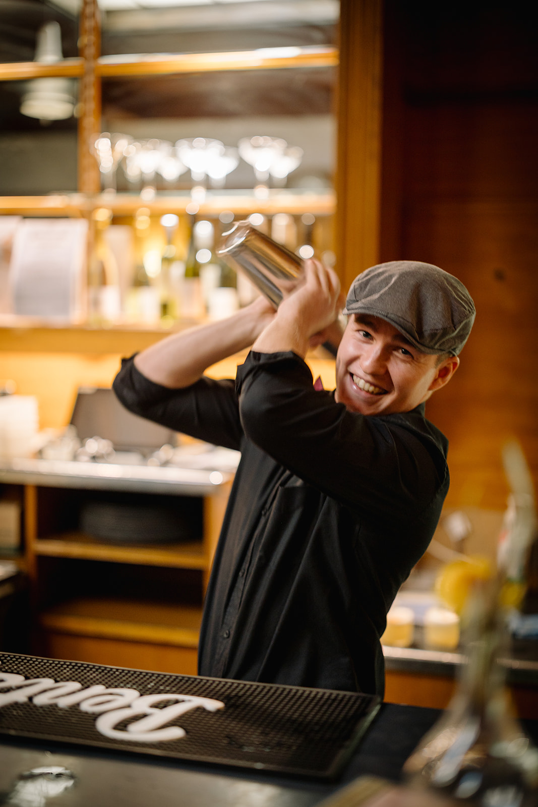A bartender from the Members' Bar shaking cocktail shakers while smiling at the camera.