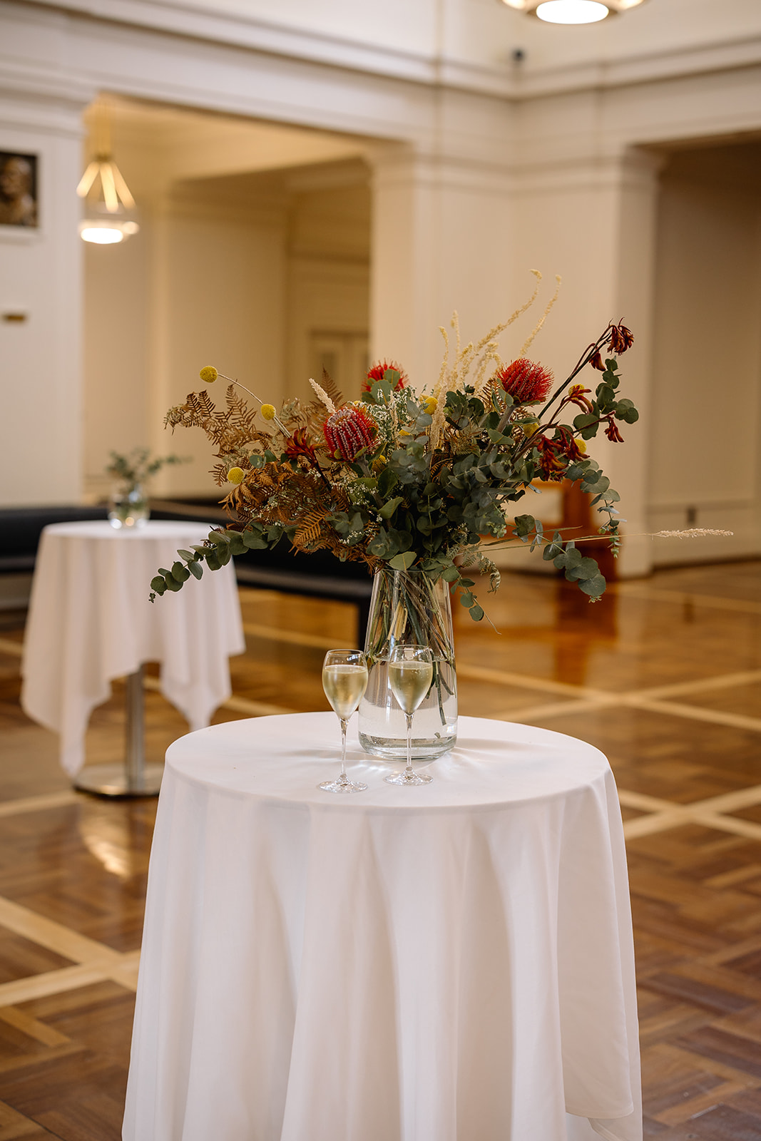 A high table in Kings Hall, with some dried native flowers in a vase and a couple glasses of wine.