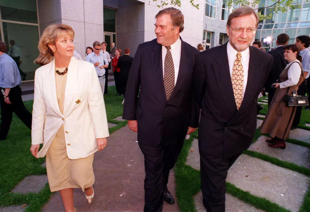 Cheryl Kernot, walks through a courtyard, exchanging a glance with Kim Beazley, Gareth Evans walking alongside them.