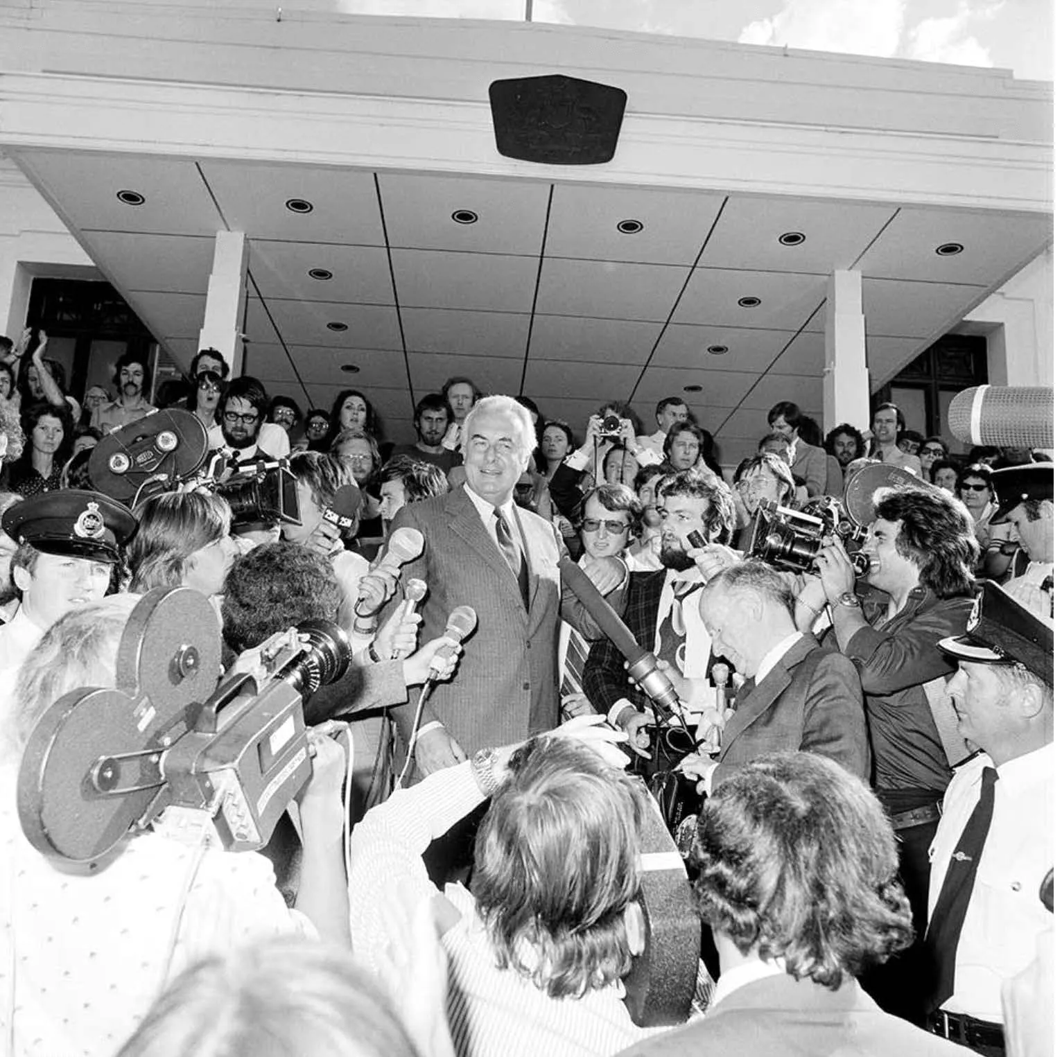 A man walking through a crowd of reporters down the Old Parliament House steps