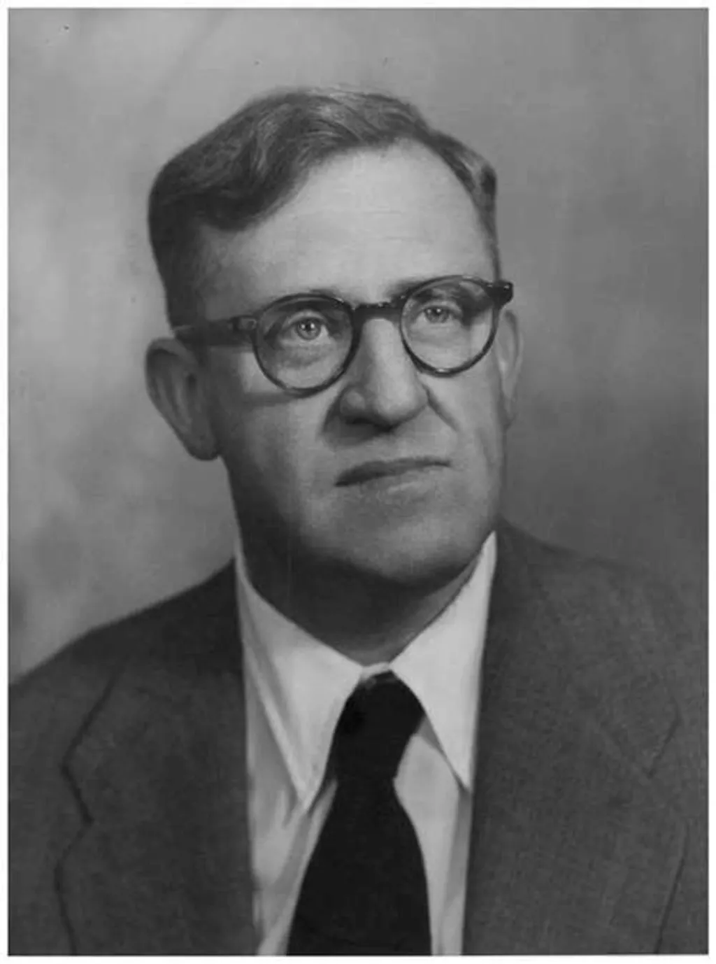 A black and white portrait photograph of Arthur Calwell, a man wearing dark-framed glasses, suit jacket and a black tie.