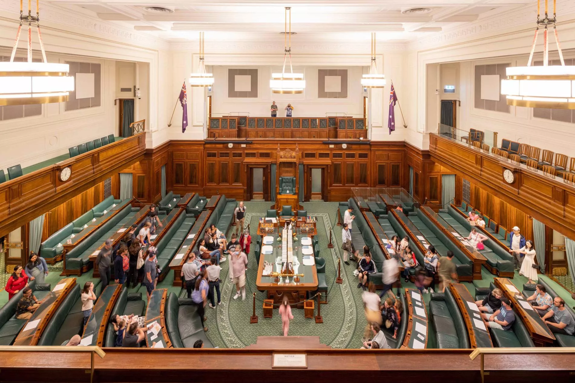 A view looking down onto the House of Representatives Chamber which has green carpet and green leather and timber benches in a U-shape surrounding a central table. 