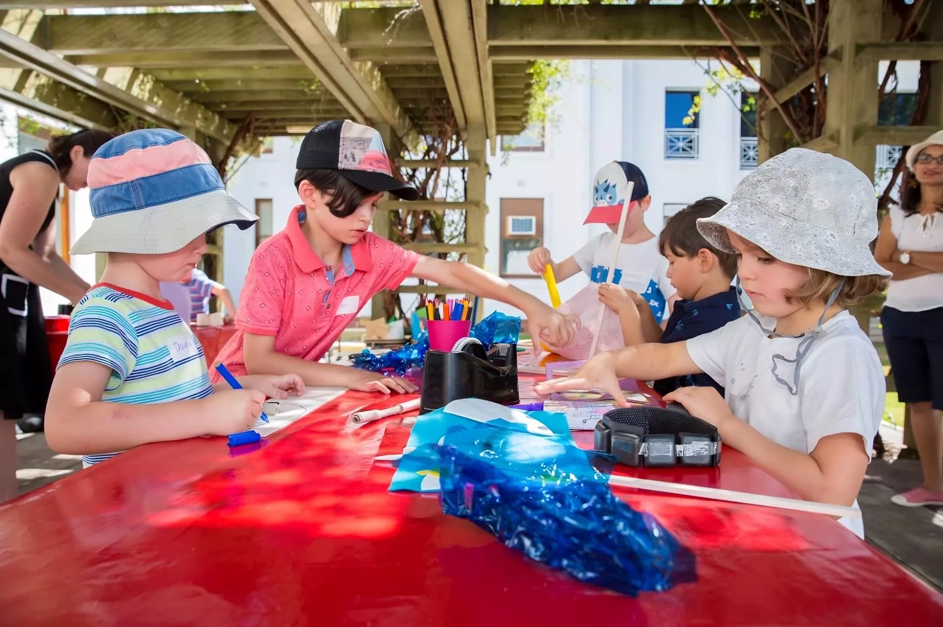 Four children stand around a table outdoors, each focusing on an idividual craft project.