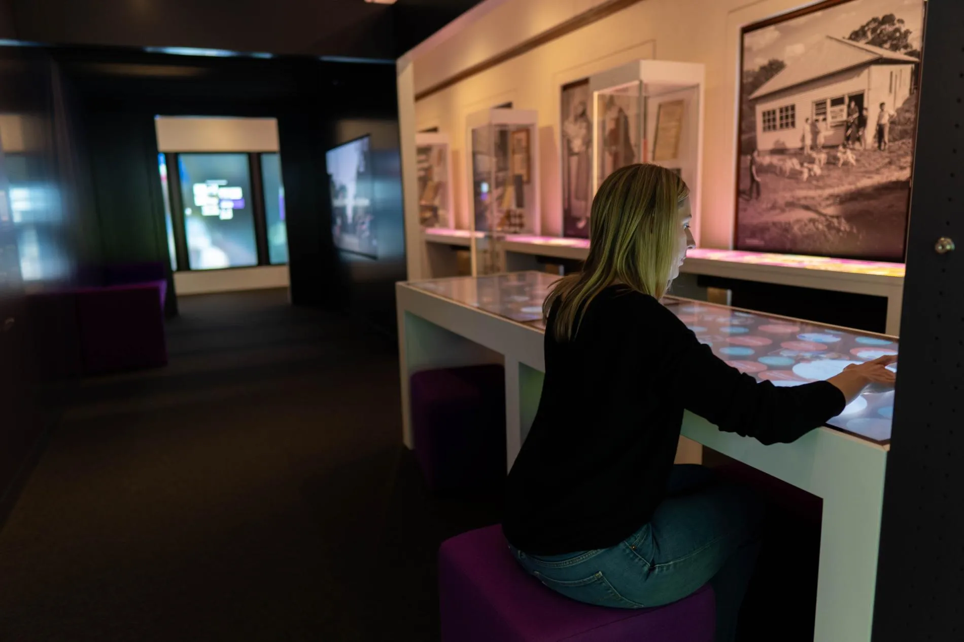 A woman is sitting and interacting with a touchscreen in an exhibition