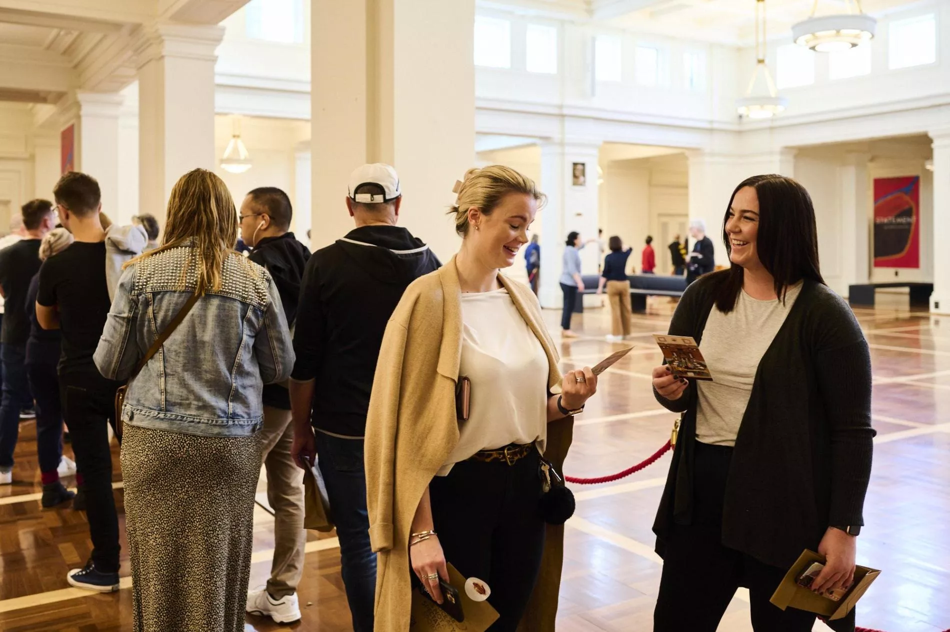 Two women talk to each other in a queue in King's Hall. 