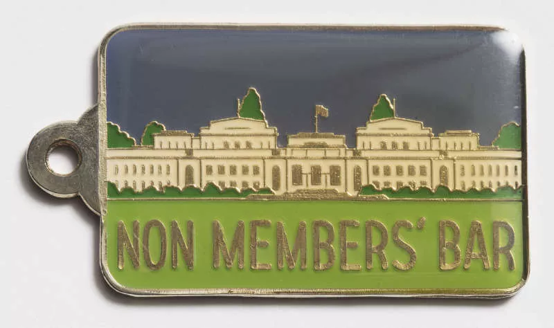 Photograph of a metal tag with an enameled illustration of Provisional Parliament House and the label "Non member's bar"