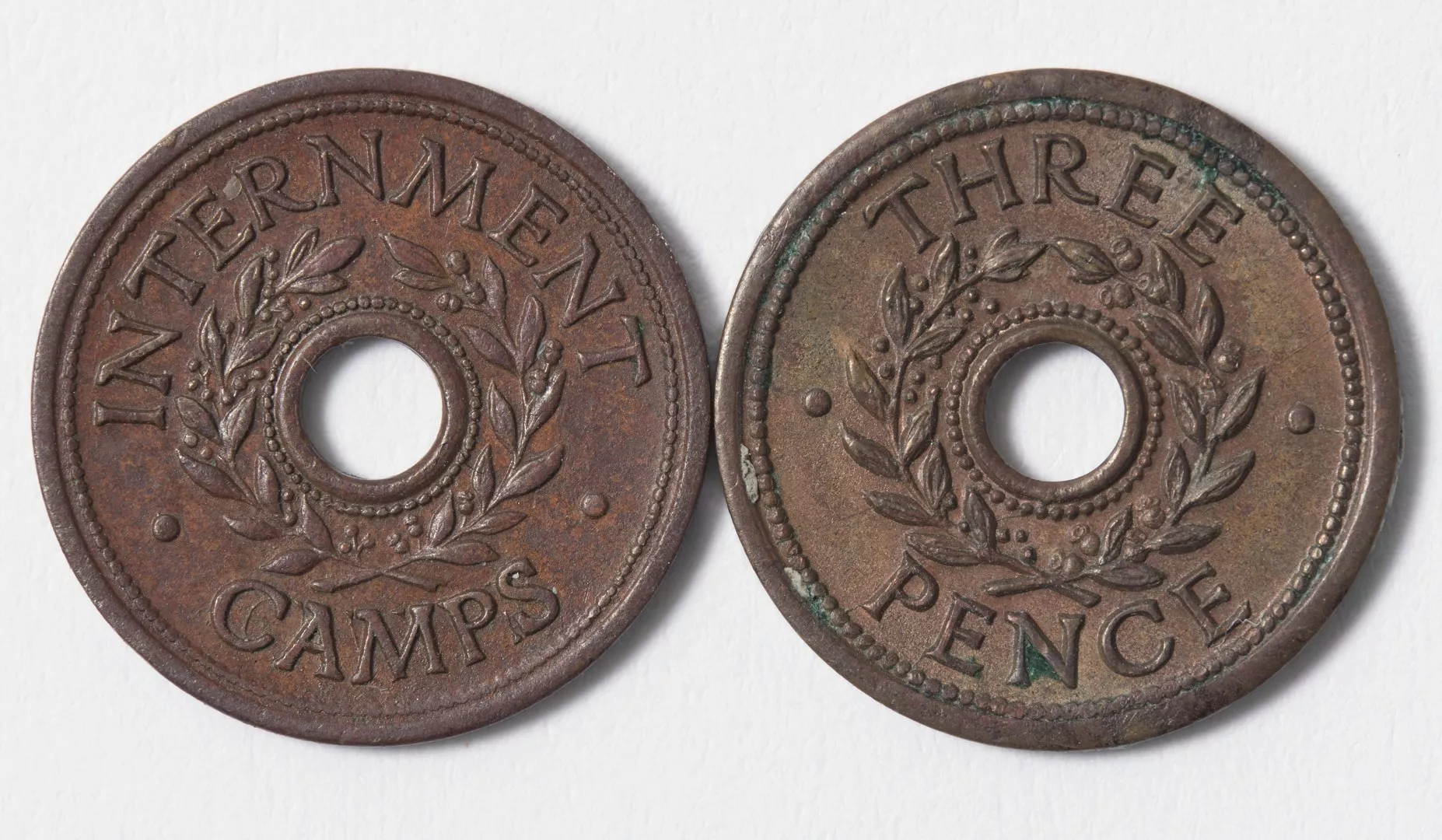 The front and back of a threepenny copper internment camp token with the words 'internment camps' and 'three pence' and featuring a wreath of eucalyptus and an olive branch.jpg